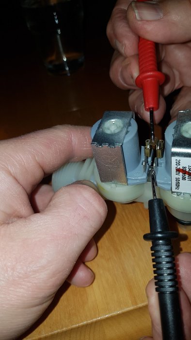 Händer som håller en elektrisk kontakt medan en multimeter testsond mäter spänning.