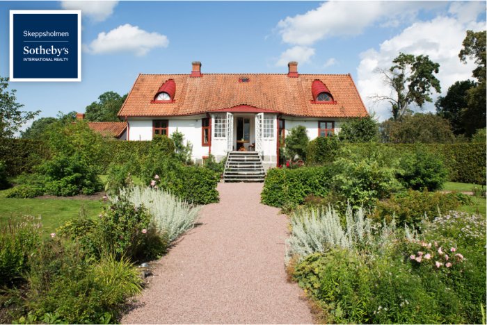 Traditionellt rött och vitt hus med unik takprofil och omgiven av en välskött trädgård.