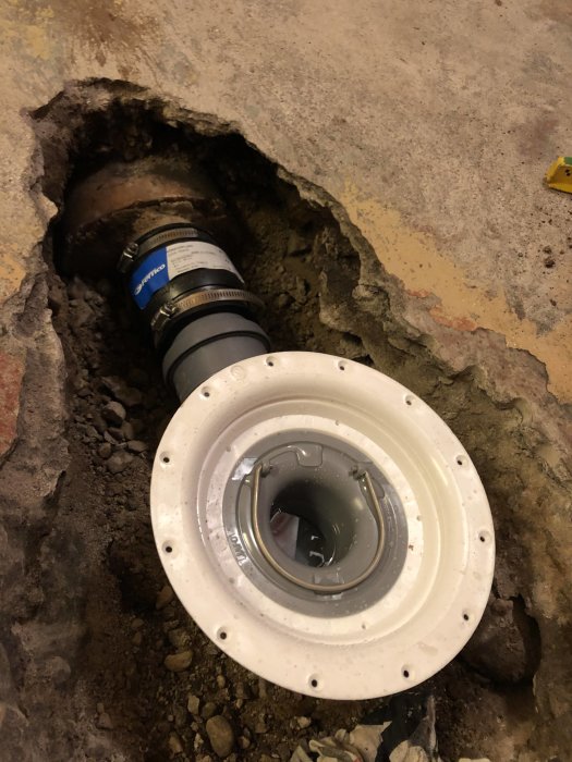 Installerad golvbrunn med ansluten avloppsrör i uppbrottet betonggolv.