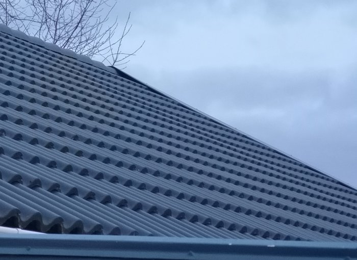 Takpannor på ett hus som visar en svag bukning neråt, mot en grå himmel i bakgrunden.