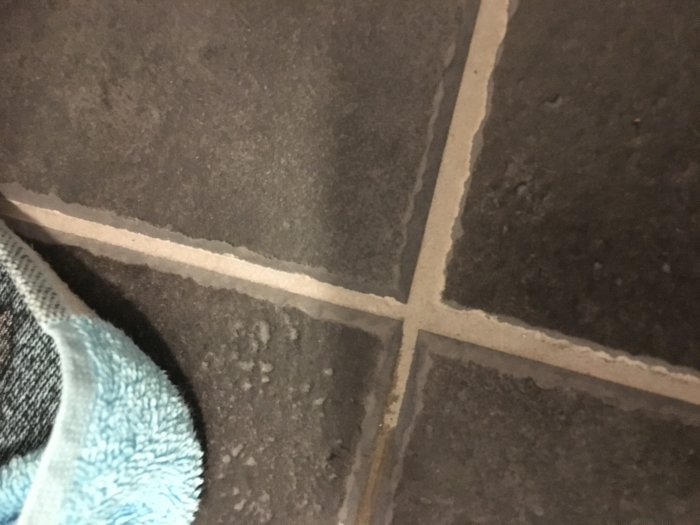 Närbild av kaklat golv med märkbara fogsprång och ojämnheter som indikerar dålig byggkvalitet.