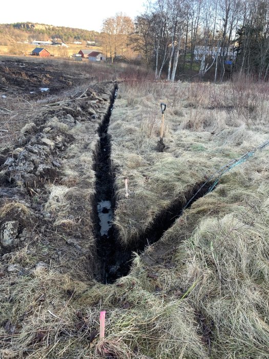 En grävd fiberkabelgröp genom en tomt med spade och markeringspinnar i kanten.