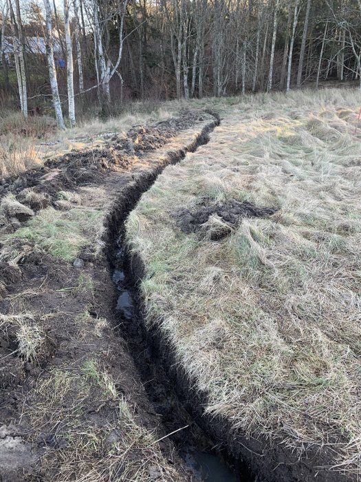 Nygrävd kabelgräv för fiber på en tomt med öppen och röjd mark i bakgrunden.