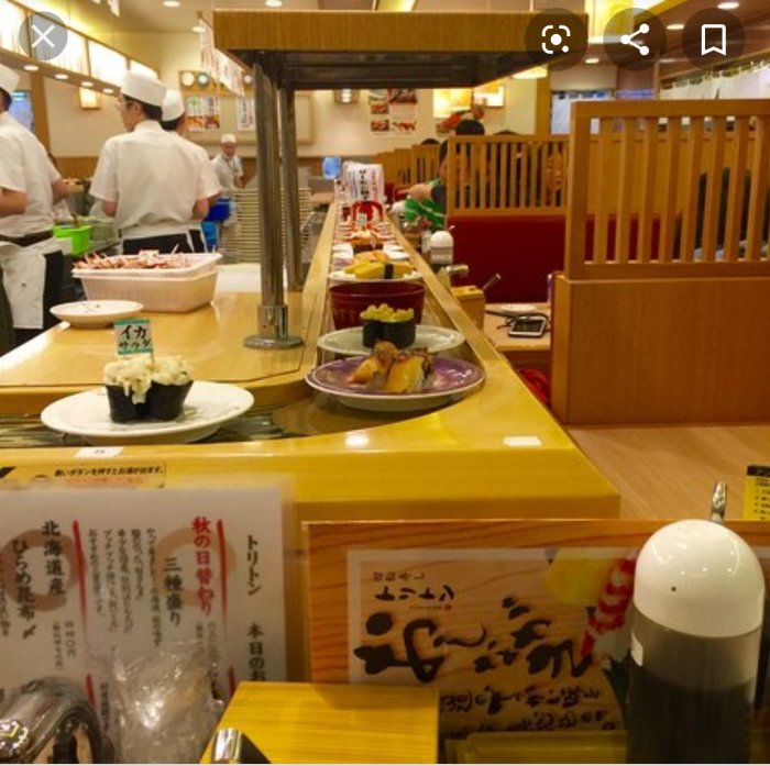 Rullband med olika sushirätter framför sittande gäster i en japansk sushirestaurang.