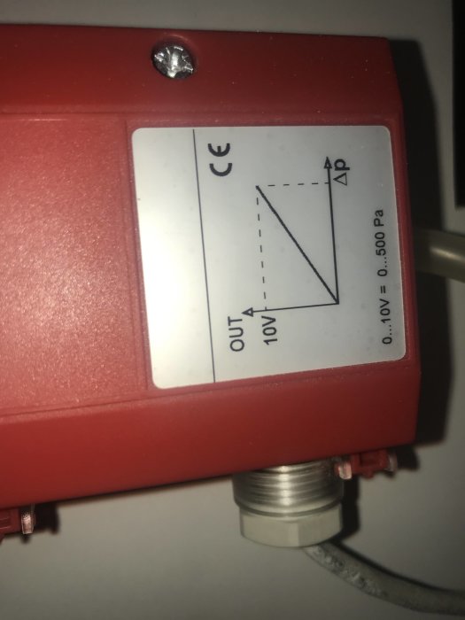 Närbild av röd apparat med CE-märkning och diagram, ansluten med kablar, potentiellt en del av ett ventilationssystem.