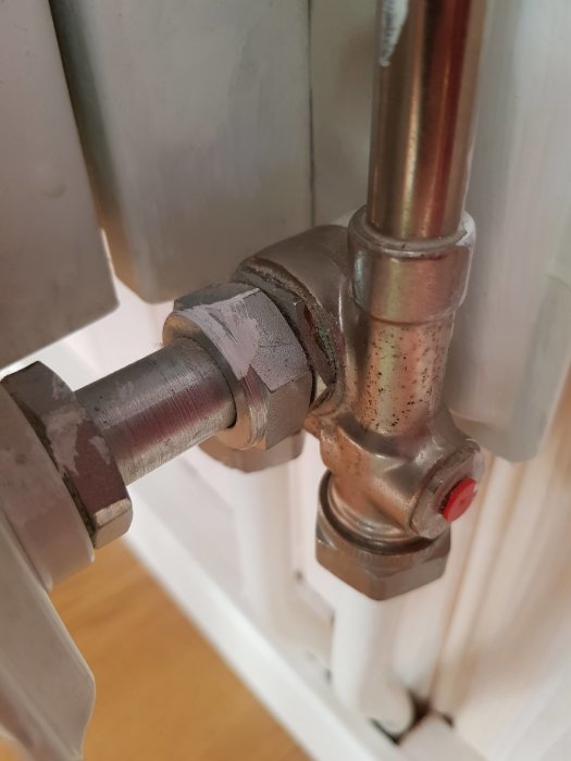 Närbild av en radiatorventil med kopparledning och avstängningsknapp mot en vit vägg.