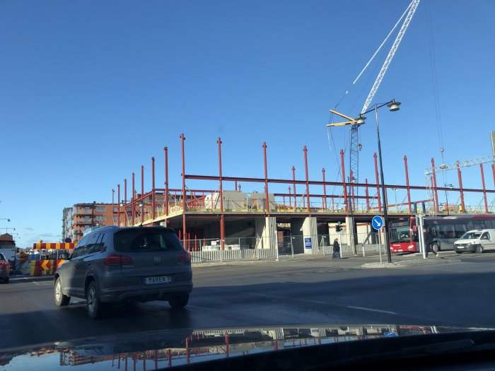 Konstruktion av en byggnad med röda stålbalkar och en kran i Karlskrona, reflekterat i en vattenpöl.