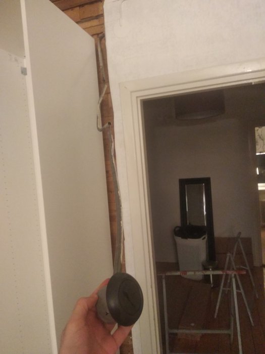 Hand håller en rund strömbrytare framför en öppen garderobsvägg med synlig elektrisk ledning och rör.