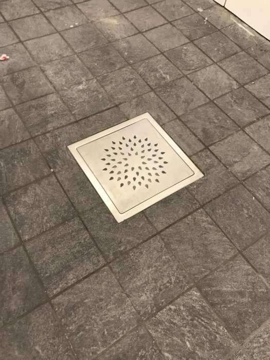 Nylagt och fogat grått klinkergolv med en fyrkantig golvbrunn i mitten.