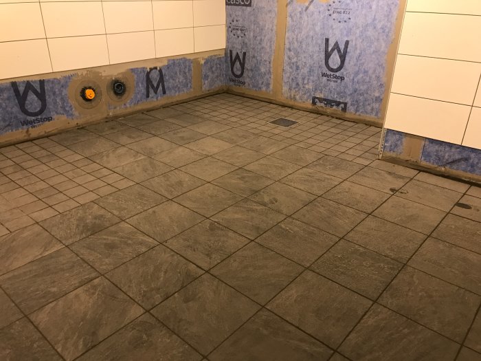 Nyinstallerat klinkergolv i en ofärdig dusch med synliga väggenheter och röranslutningar.