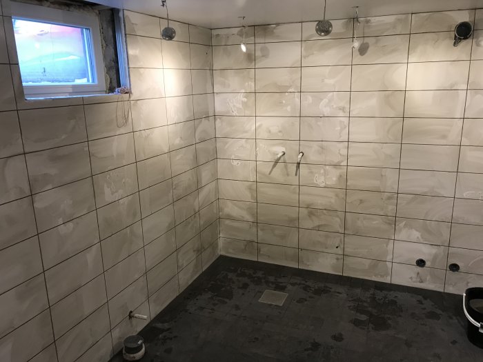 Ej färdigställt badrum med nya kakelväggar och installerade duschdetaljer men utan golv och fondvägg.