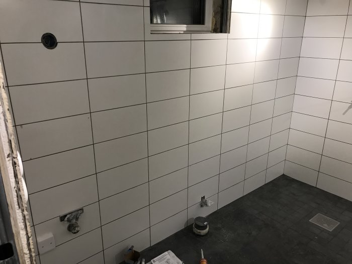 Renoverat badrum med nya vita kakelväggar och mörkt kaklat golv.