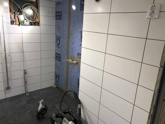 Renoverat badrum med halvfärdig kakelsättning, verktyg på golvet och oisolerade väggar.
