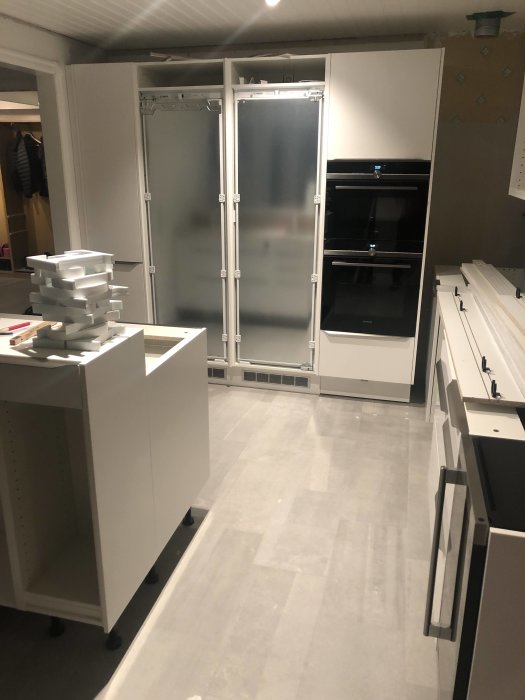 Renoverat kök med vita skåp och inbyggda ugnar under konstruktion.