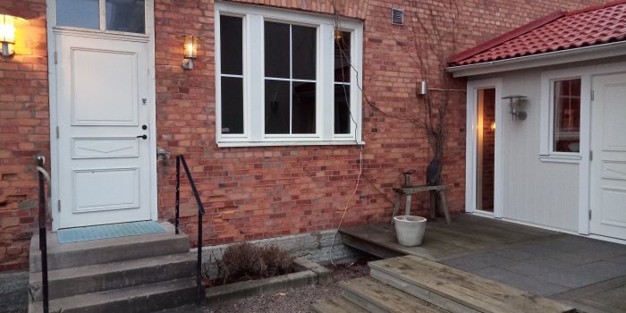 Gamla tegelbyggnadens exteriör med en vit dörr och fönster, före renovering till tvättstuga/badrum.