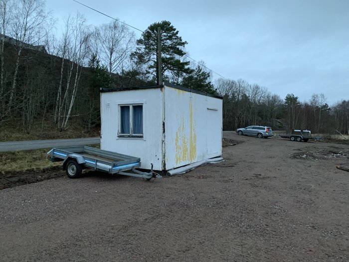 Arbetsbod placerad på en byggplats med släpvagn framför och bilar i bakgrunden.