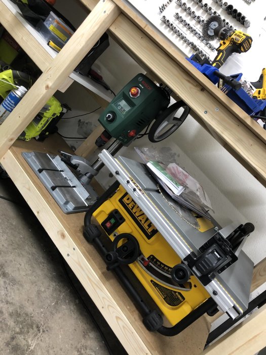 Verkstadsbänk med en Bosch borrstation och DeWalt kapsåg, diverse verktyg och borruppsättningar i bakgrunden.