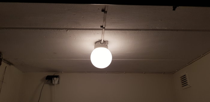 Kellarin katto, jossa on valkoinen pyöreä lamppu oikealla puolella ja sähköjohdot kulkevat katon suuntaisesti.