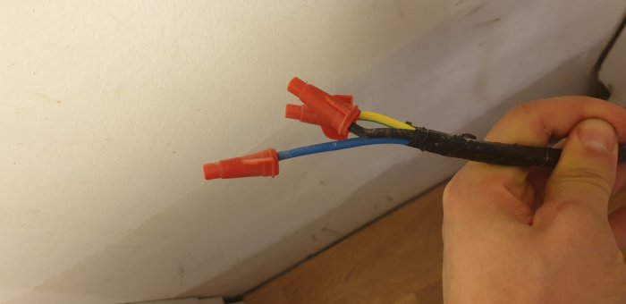 En hand håller okopplade elektriska kablar med kabelskor redo för anslutning.