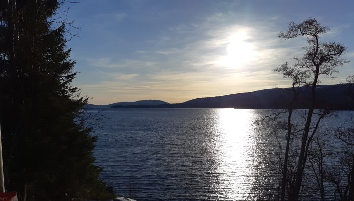 Solnedgång över en sjö med silhuetter av träd och kullar i bakgrunden.