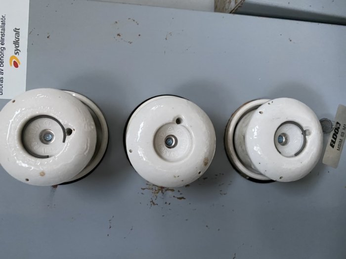 Tre vita keramiska säkringar på en grå yta, eventuellt från ett proppskåp.