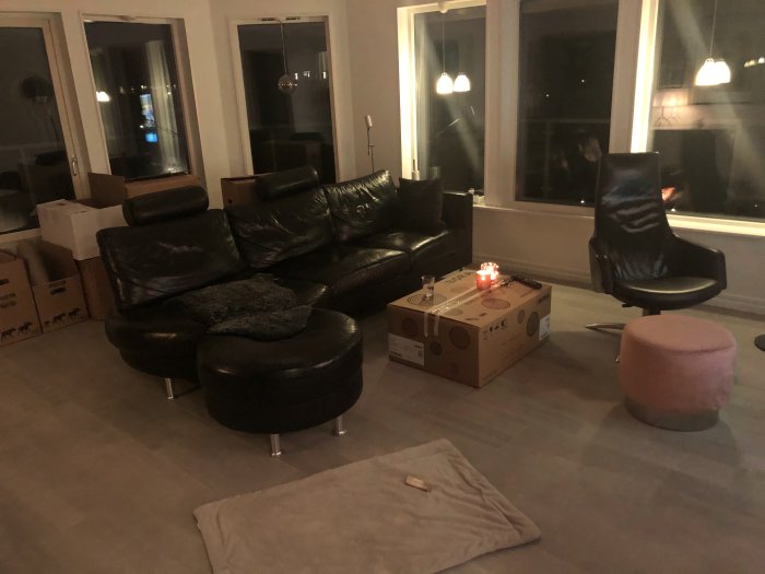 Vardagsrum under uppackning med soffgrupp, kartonger och en tänd ljuslykta på ett bord.