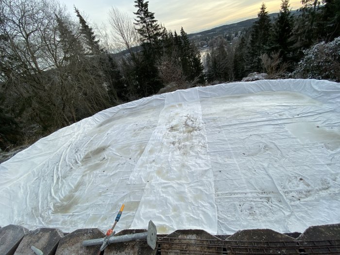 Plastduk täcker en backe med skogslandskap i bakgrunden och inga tecken på kyla.