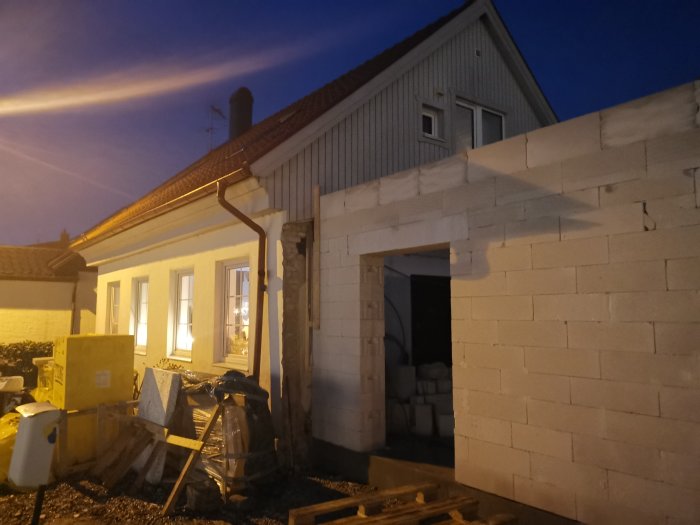 Hus under renovering på kvällen med nybyggd vägg av lättbetongblock och byggmaterial framför.