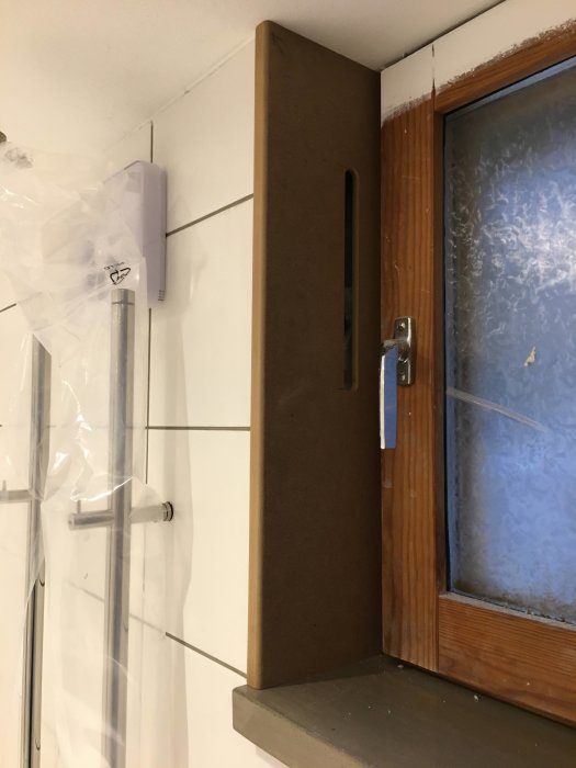 Nyinstallerad fönstersmyg vid ett frostglasfönster med fräst ventilationsspår täckt av myggnät.