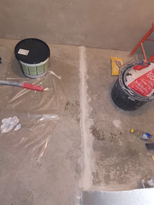 Reparation av en spricka i betonggolv med husfix och verktyg, samt spackelhinkar runtomkring.