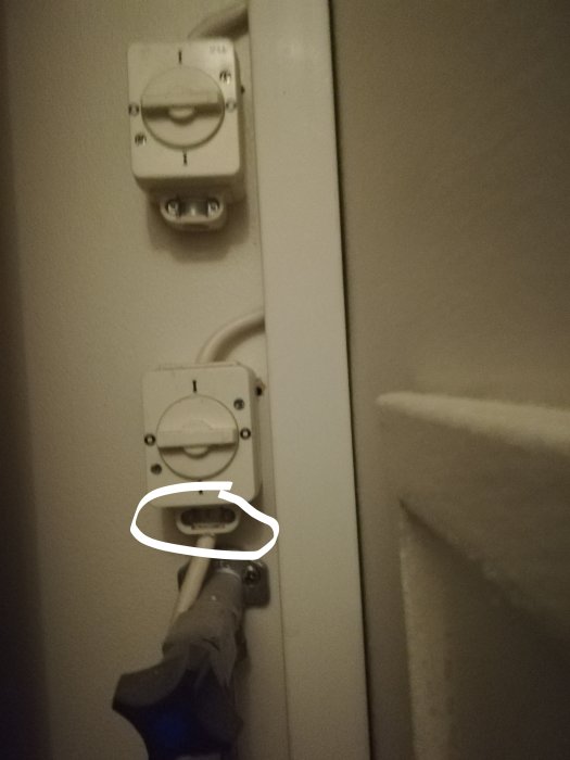 En strömbrytare och dess kabelanslutning på en vägg, med två skruvar markerade för demontering.