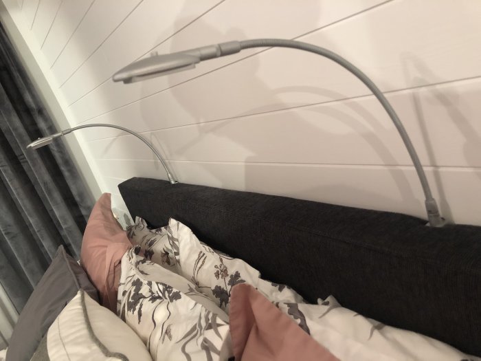Renoverat sovrum med ny sänggavel, väggpanel och moderna flexibla läslampor på väggen.