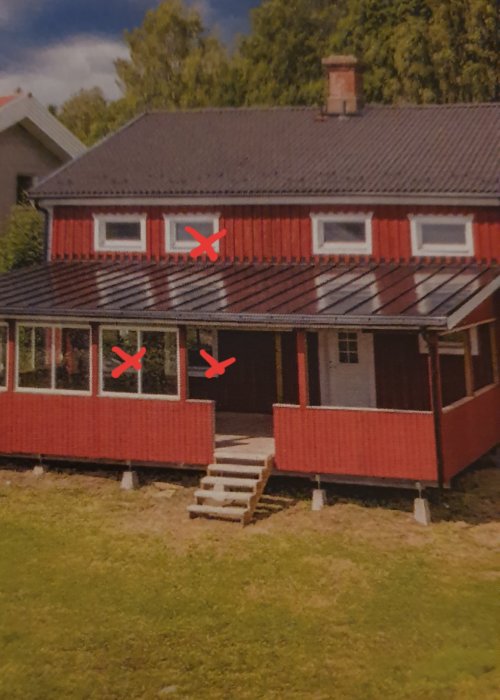 Rödmålat hus med korsmärken på fönster som indikerar läckage, värst på nedervåningen.