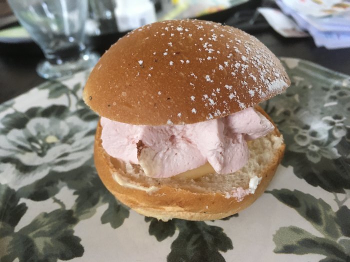Hallonsemla med vaniljkräm och rosa hallonmousse på ett blommigt underlag.