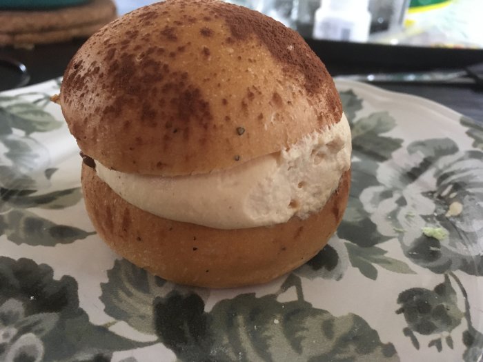 En kreativ variant av en svensk semla med grädde mellan två halvor av bröd, på ett blommigt fat.