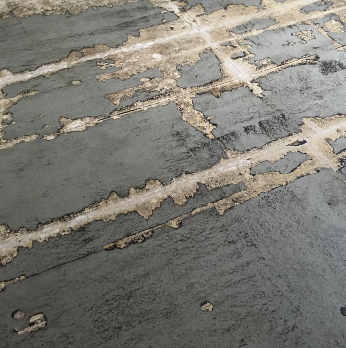 Gammalt, möjligen svartlim, på ett betonggolv med rester av lim och slitna spår.