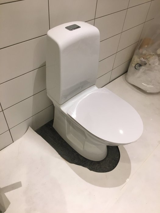 Nyinstallerad vit toalettstol i ett badrum under renovering med kaklade väggar och skyddsplast.