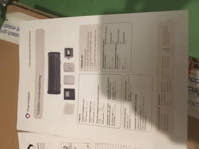 Kartong med bild och information om en Thermodrive trådlös rumsterereglering, ligger på ett bord, bilden är tagen uppifrån.