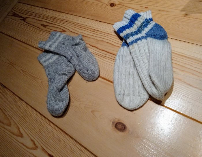 Ett par grå och ett par vit-blå stickade yllesockar på trägolv, symboliserar gamaldags golvvärme.