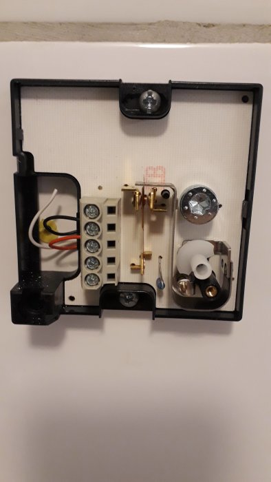 Öppen termostat med synliga kablar och komponenter på en vägg som en del av ett vattenburet golvvärmesystem.