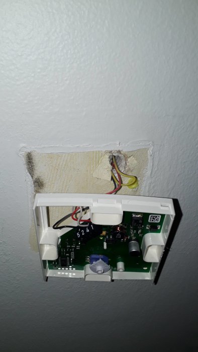 Öppen rumstermostat utan frontpanel som visar kretskort och ledningsanslutningar på vägg.