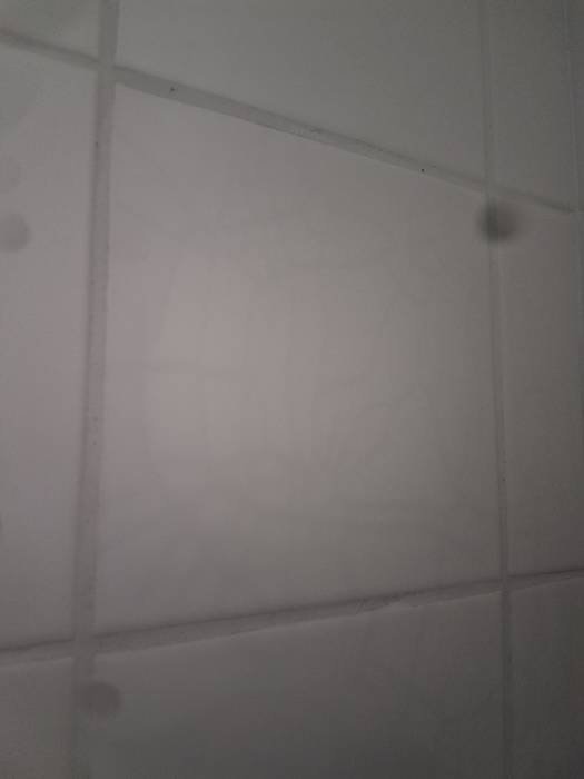 Vit kakelvägg i dusch med synliga kalkavlagringar och smuts.