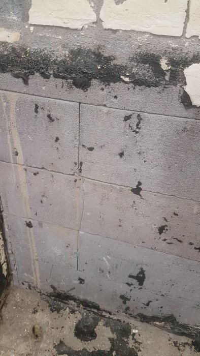 Närbild på en gammal vägg av blåbetong med sprickor och lösa block i ett badrum under renovering.