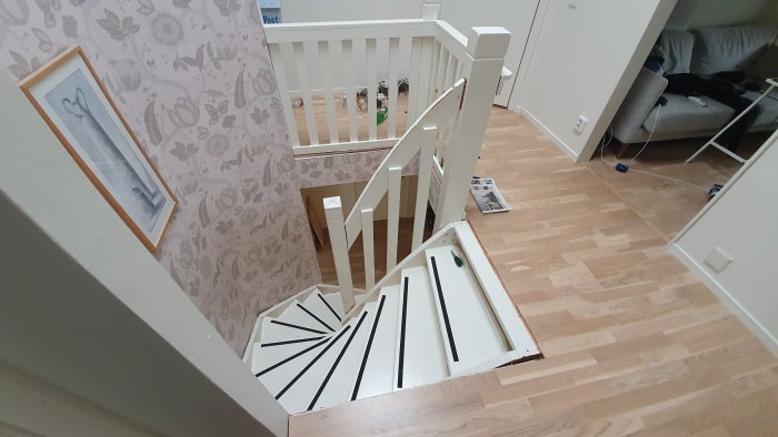En delvis demonterad vit trätrappa inomhus med synliga vitlackerade vangstycken och lösa svarta streck som mallar.
