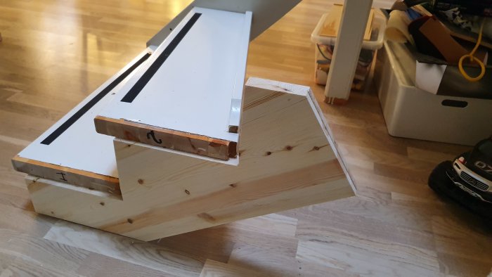 En provkonstruktion av en trappstegsdel med en vitlackerad yta och synlig trästruktur, placerad på ett golv.