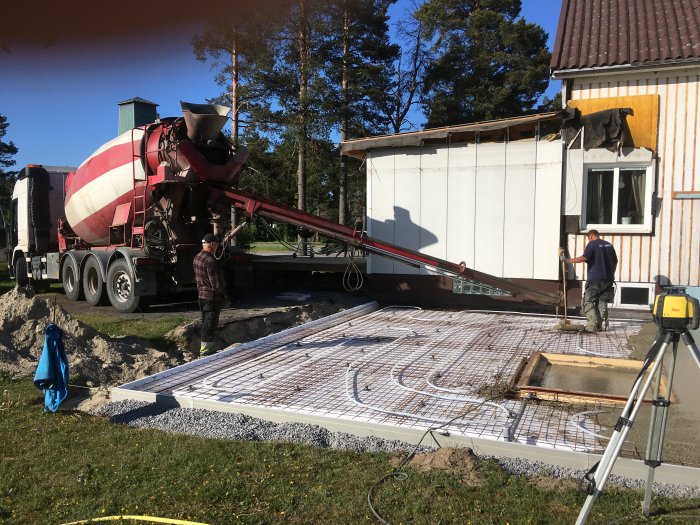 Betong gjuts för en nedfälld garageplatta med förstärkt kant nära en armeringsjärn och avloppsgrop.