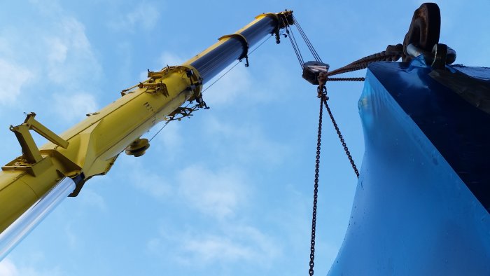 Gul kran som lyfter blått föremål mot en klarblå himmel.