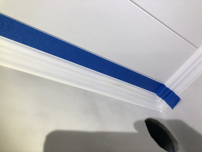 Vitmålad taklist som är maskerad med blå tejp mot ett vitt innertak, redo för fogning.