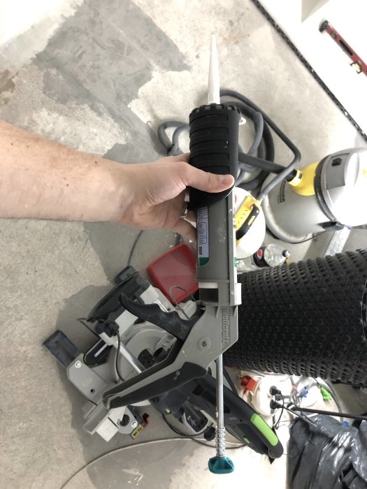 Fogpistol med MS Polymer tub i en hand framför verktyg på ett ojämnt betonggolv.
