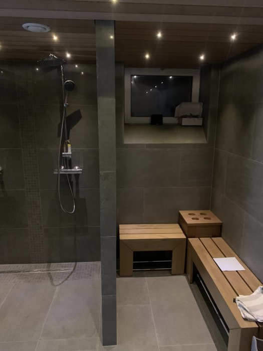 Nyrenoverat badrum med inbyggd dusch, sittbänkar i trä och infällda taklampor.